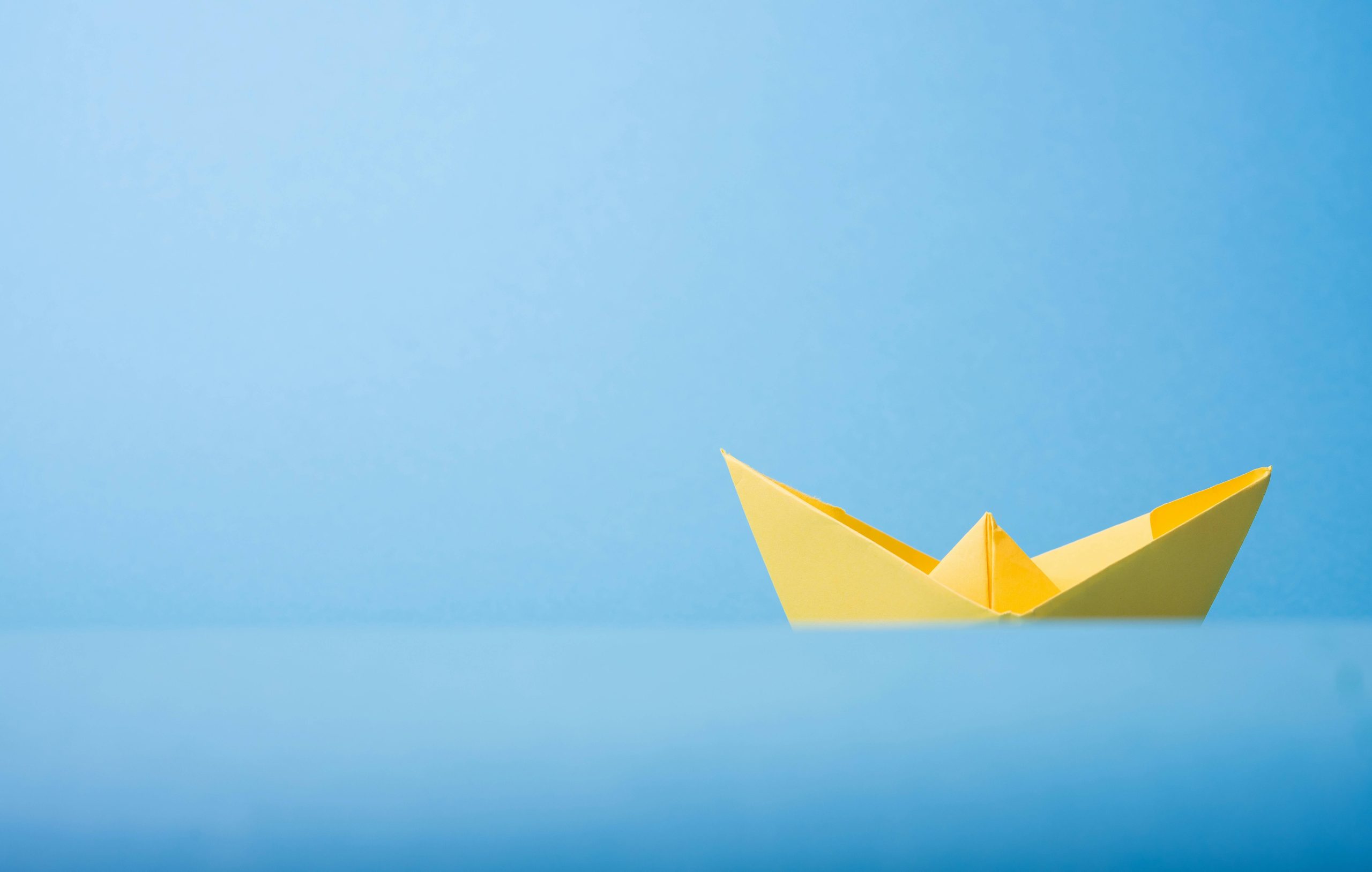 Yellow Paper Folded into Shape of Boat Against Light Blue Paper Background